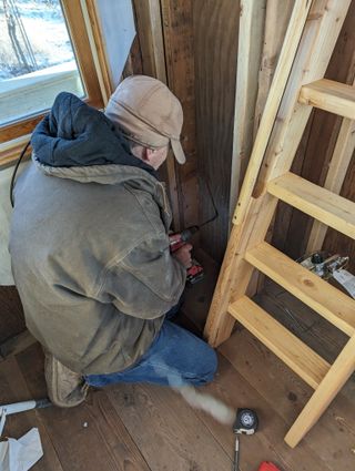 Dad drills a hole into the cabin where the conduit will go through